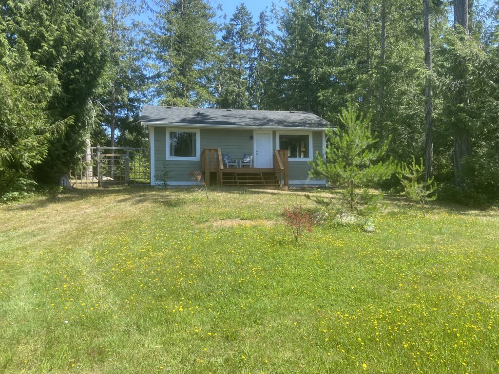 A view of the cottage from the backyard. The unpainted wood rear deck can be seen with it's stairs leading up to floor level.