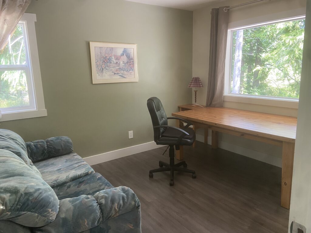 The second bedroom of the cottage, with a large table in front of the main window and hide-a-bed opposing it