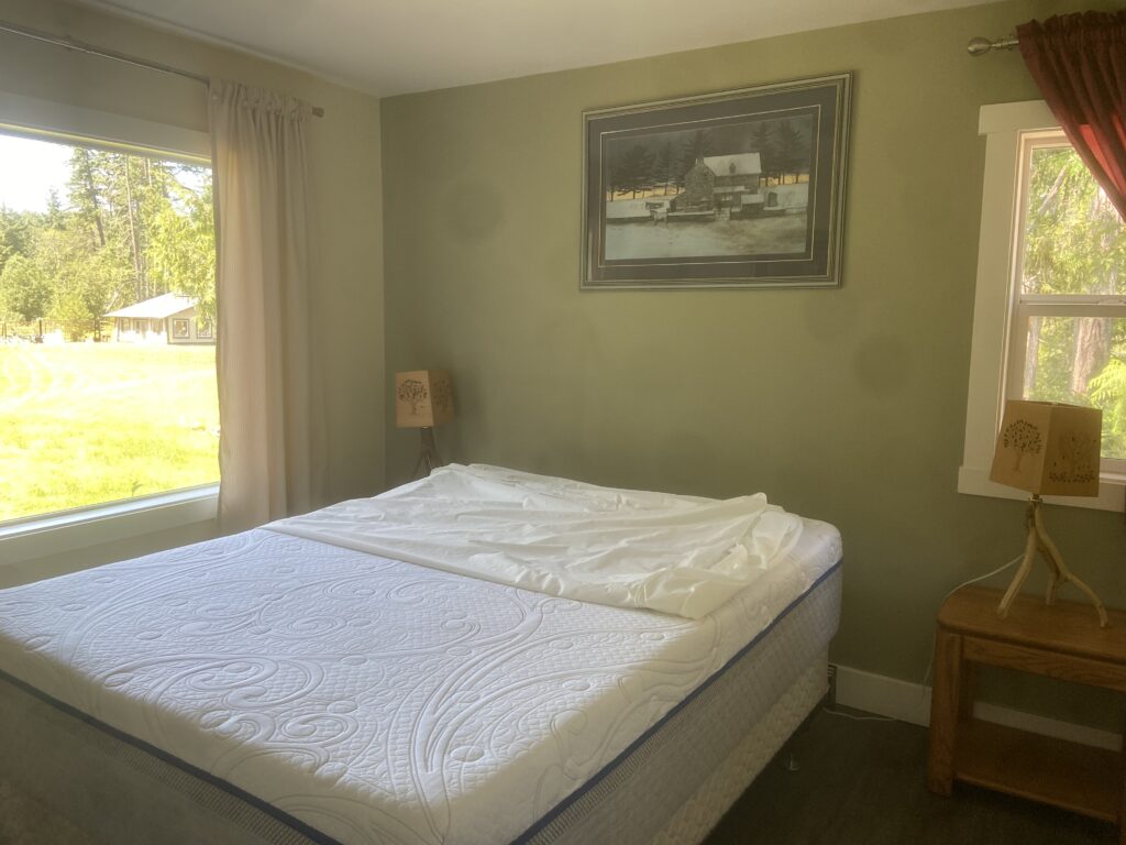 The master bedroom of the cottage, with a large bed and large window with views of the yard and Conservatory